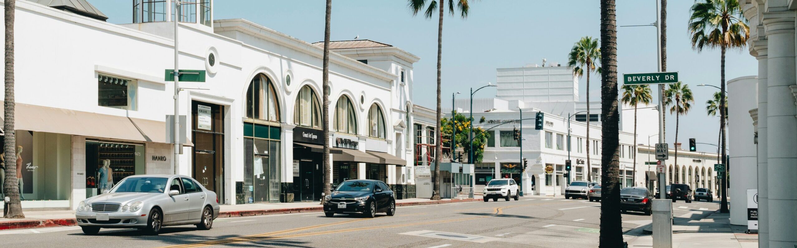 Palm tree-lined commercial street in Los Angeles with large storefront windows and white buildings on Beverly Drive